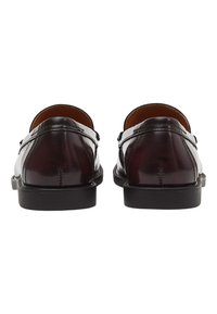 Braune Leder-Loafer mit glänzender Oberfläche, ausgestattet mit einer niedrigen schwarzen Sohle, genähten Details und einer abgerundeten Hinterseite. Keine auffälligen Beschläge.