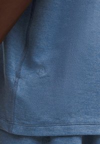 Blå sports top lavet af blødt stof, med et rundt logo på den nederste kant, synlige stikninger og et afslappet pasformdesign.
