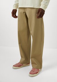 Beige wide-leg trousers made of cotton blend, featuring a smooth texture. Paired with pink sneakers, showcasing a casual, relaxed fit.