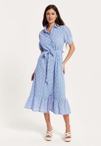 Light blue dress with short puff sleeves, a tie waist, and a ruffled hem. Features an all-over intricate pattern and a button-up front.