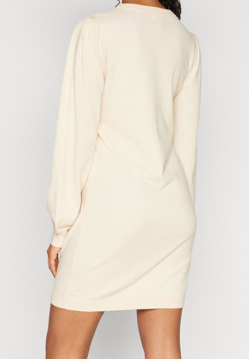 Robe pull couleur crème avec des manches longues, texture douce, encolure ronde et léger détail bouffant aux épaules ; silhouette ajustée.