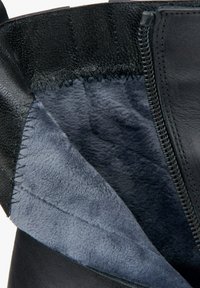 Wnętrze czarnej skórzanej botki z miękkim szarym polarem, widocznymi detalami szwów oraz zamkiem błyskawicznym z boku.