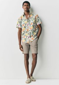Kortærmet blomsterskjorte med orange og grønne mønstre; parret med lysebeige shorts og brune loafers. Glat stof, afslappet pasform.