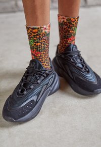 Czarne sportowe sneakersy o teksturowanej powierzchni, gładkich akcentach i grubej podeszwie. Połączone z kolorowymi skarpetkami w wzory, z motywami kwiatowymi i lamparta.