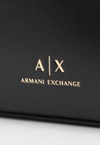 Sac en cuir noir avec le logo doré embossé "A|X ARMANI EXCHANGE", texture lisse et design minimaliste.