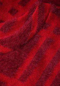 Rote Strickstoff, der eine Mischung aus glatten und flauschigen Texturen mit diagonalen Streifen und subtilen Mustern in dunkleren Farbtönen zeigt.