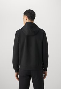 Felpa con cappuccio nera dal tocco morbido, con polsini e vita a coste. Presenta un taglio di lunghezza media e un design semplice e senza cuciture.