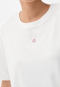 Biała bawełniana koszulka z okrągłym dekoltem i krótkimi rękawami, z minimalistycznym haftowanym wzorem w czerwieni i bieli na lewej piersi.