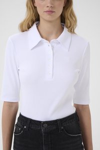 Λευκό ριμπ πουκάμισο πόλο με ανοικτό γιακά, κουμπώματα μπροστά και κοντά μανίκια. Διαθέτει διακριτική λεπτομέρεια με λογότυπο. Φορεμένο με μαύρο τζιν.