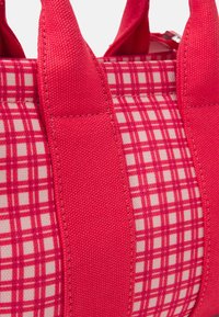 Sac en tissu rouge avec un motif à carreaux et des panneaux latéraux rouges doubles. Dispose de poignées en textile robustes et d'un design lisse et structuré.