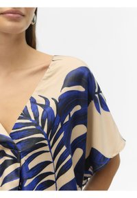 Losse blouse in crème met een marineblauwe tropische bladerenprint. Heeft een diepe V-hals en korte mouwen. Zijdezachte textuur.