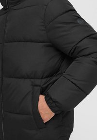 Giacca nera imbottita con design trapuntato, zip frontale, tasche laterali e polsini a coste, realizzata in un tessuto morbido e isolante.