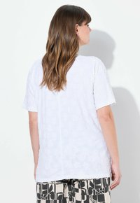 Top bianco a maniche corte caratterizzato da un tessuto testurizzato, scollatura rotonda e una vestibilità ampia. Sul retro presenta un dettaglio di cucitura centrale.