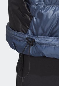 Ourlet de veste matelassée bleue et noire avec cordon de serrage réglable et bouton sur vêtements noirs.
