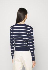 Sweter w granatowo-białe paski, z ribbowanymi mankietami i dolnym wykończeniem, okrągły dekolt, dopasowany krój, gładka tekstura. Noszony z jasnymi spodniami.
