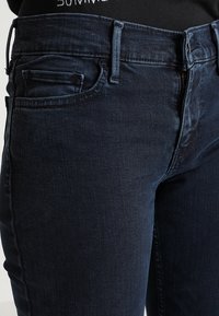 Mörka denimjeans med en slim fit. Funktioner inkluderar dragkedja, bältesslingor och framfickor. Tyget har en slät textur.