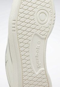 Semelle de chaussure Reebok avec motif de bande de roulement en forme de diamant, zone de prise circulaire, bords texturés et logo "Reebok" embossé sur une semelle extérieure en caoutchouc écru.