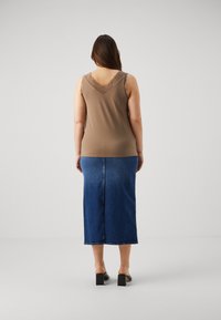 Brun bluse uten ermer med blonder, kombinert med et langt denimskjørt. Antrekket har en tettsittende silhuett og teksturerte materialer.