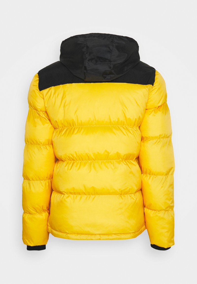 Veste matelassée jaune avec des accents noirs sur les épaules, dotée d'une capuche, d'une texture matelassée et de poignets élastiques. Légère et conçue pour la chaleur.
