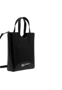 Sac fourre-tout en cuir verni noir avec deux poignées et une bandoulière amovible, orné du logo argenté « Karl Lagerfeld Jeans » sur le devant.