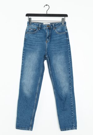 Jean bleu taille haute à jambe droite suspendu sur un cintre noir sur fond blanc.