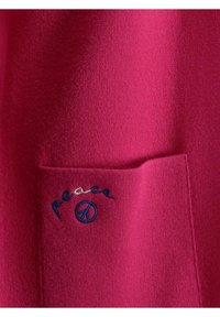 Maglione fucsia con una texture morbida, con un ricamo della parola "pace" e del simbolo della pace blu sulla tasca anteriore.