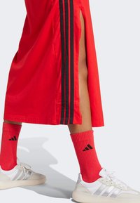 Red athletic skirt with black side stripes, paired with red ribbed socks featuring black logo, and white sneakers with gray accents.