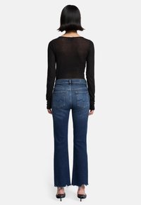 Dopasowana czarna bluzka z długim rękawem i ciemnoniebieskie jeansy dzwony z postrzępionymi brzegami, posiadające dwie tylne kieszenie i wysoki stan.