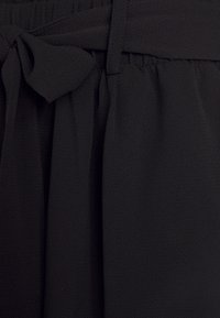 Czarne spodnie z tkaniny o teksturowanym wykończeniu, z wiązaniem w talii i plisowanym wzorem dla zwiększonej objętości. Miękka, lekka tkanina.