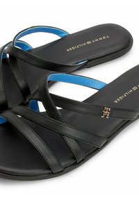 Svarta sandaler med korsade remmar av läder, med en blå accent och en metallisk logodetalj. Platt sula med jämn yta.