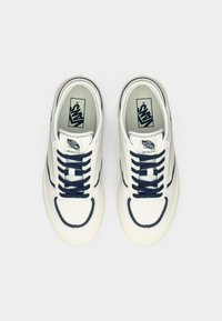 Λευκό αθλητικό παπούτσι με ναυτικά μπλε στοιχεία, υφή στο πάνω μέρος, στρογγυλή μύτη, επίπεδα λευκά κορδόνια και λογότυπο Vans στη γλώσσα. Επίπεδη σόλα με διακριτικό σχέδιο.