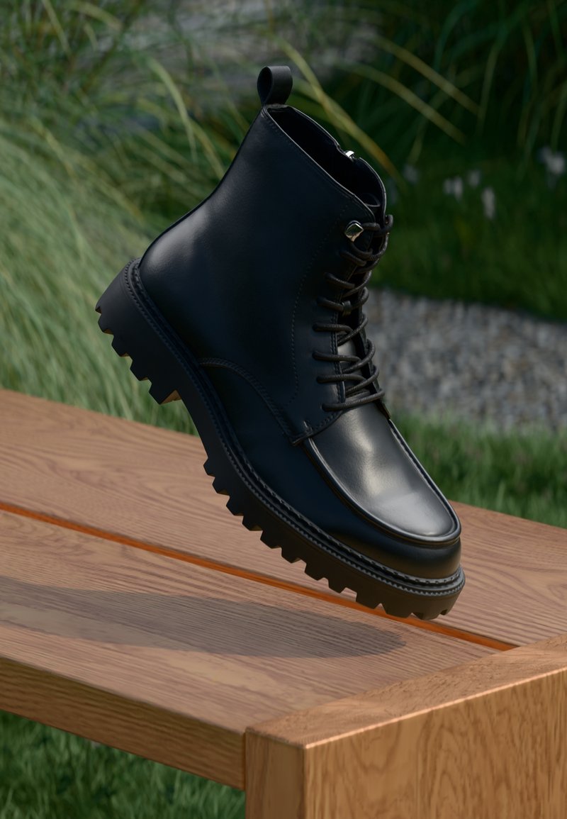 Botte noire en cuir à lacets avec une semelle épaisse à crampons, équilibrée sur le bord d'un banc en bois à l'extérieur avec de l'herbe en arrière-plan.