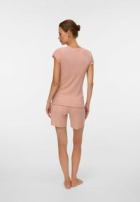 Femme debout pieds nus, vue de dos, portant un ensemble assorti rose pâle composé d'un haut à manches courtes et d'un short avec des ourlets festonnés.