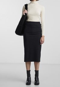 Col roulé crème à côtes, jupe crayon noire à rayures, et bottines noires. Les accessoires incluent un sac à épaule noir en tissu texturé.