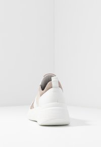 Baskets blanches et beiges vues de dos sur une surface blanche avec un fond blanc uni.