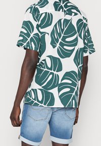 Camicia a maniche corte realizzata in tessuto leggero, con uno sfondo bianco e grandi motivi di foglie verdi. Con una vestibilità casual.