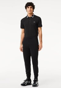 Zwarte polo met een contrasterende witte kraag, gecombineerd met zwarte trainingsbroek en zwarte sportschoenen met een gestructureerd ontwerp.