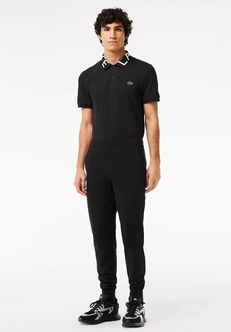 Zwarte polo met een contrasterende witte kraag, gecombineerd met zwarte trainingsbroek en zwarte sportschoenen met een gestructureerd ontwerp.