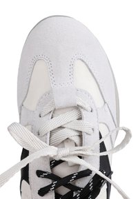 White and black sneaker with white and black laces, tied in a bow, showing the textured suede and stitching details on the toe area.
