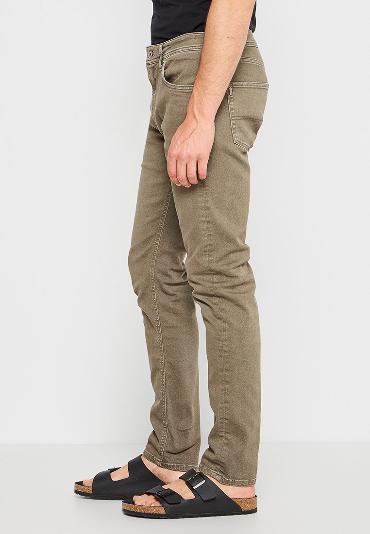 Jeans color caqui con un corte ajustado, diseño de cinco bolsillos y detalles cosidos, acompañados de sandalias negras con hebillas ajustables.