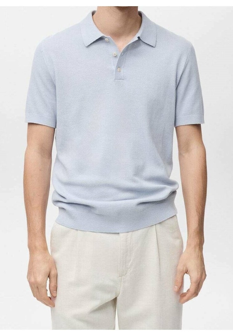 Homme portant un polo bleu clair à manches courtes rentré dans un pantalon beige, debout avec les bras détendus le long du corps.