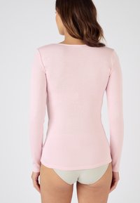 Camicia a maniche lunghe di colore rosa chiaro, con texture a coste, design aderente e scollatura rotonda. Tessuto morbido, dettagli di cucitura minimi e orlo curvo.