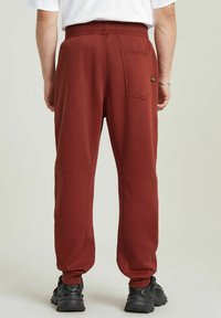 Bordeauxkleurige joggingbroek van zachte stof, met een enkele achterzak en taps toelopende boorden. De tailleband is elastisch voor extra comfort.