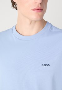 Světle modré tričko s krátkým rukávem vyrobené z měkké tkaniny, s kulatým výstřihem a tmavě modrým logem "BOSS" vyšitým na hrudi.