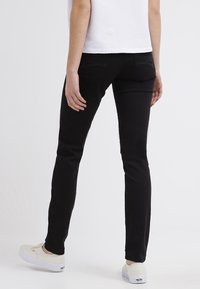 Černé kalhoty s úzkým střihem, vyrobené z měkké, pružné tkaniny. Mají zadní kapsy a hladký povrch. Kombinované se světlými botami.