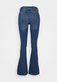 Calças de ganga azuis de corte à boca de sino com uma cintura de altura média, dois bolsos traseiros e uma textura suave. O tecido apresenta um leve desbotamento e detalhes de costura.