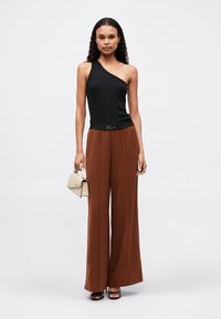 Top negru cu o singură umăr, asortat cu pantaloni largi maro cu talie înaltă, accesorizat cu o geantă mică bej și sandale negre cu toc.