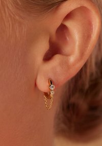 Gold hoop earring with two clear gemstones and a delicate chain accent, featuring a smooth finish and a rounded design.
