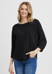 Schwarzer strukturierten Pullover mit weitem Halsausschnitt und Dreiviertelärmeln, kombiniert mit blauen Jeans. Lässige Passform mit abgerundetem Saum.
