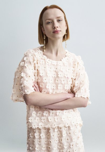 Haut et jupe fleurie rose pâle, en tissu transparent avec des appliqués de fleurs en couches, dotés de manches courtes et d'un col rond.